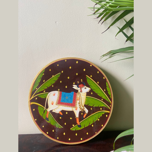 Nilah Collective  Handpainted Picchwai Wall Plate- dark brown cow with banana leaf