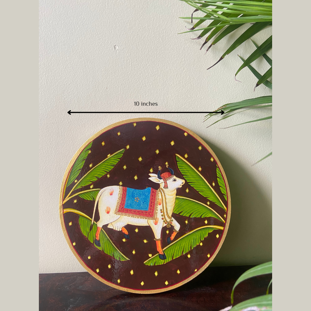 Nilah Collective  Handpainted Picchwai Wall Plate- dark brown cow with banana leaf